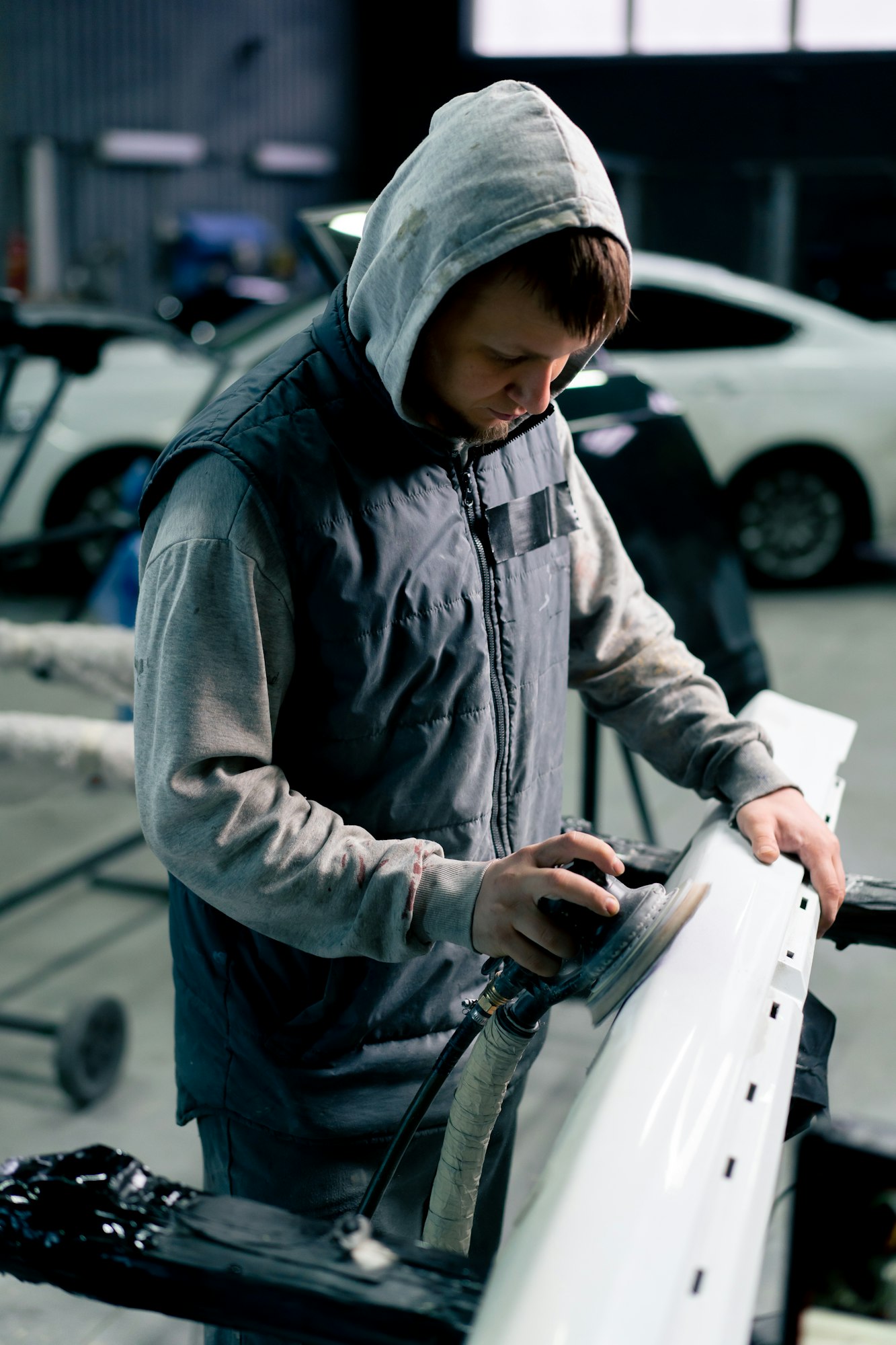 auto mechanic at a service station polishing the front part of white car